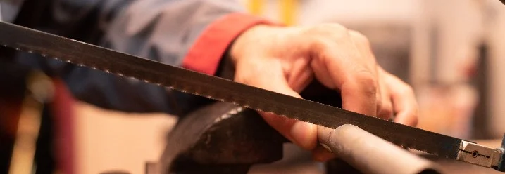 Hand sägt Metallrohr mit Säge.